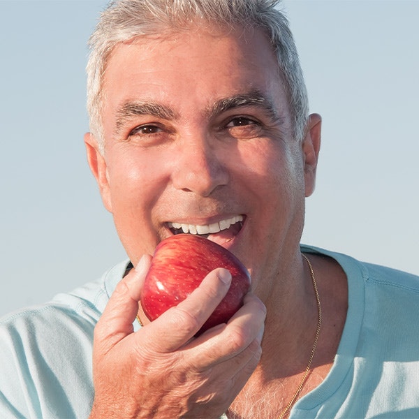 Happy man biting into an apple, demonstrating strong dental implants placed by Dr. Schlaikjer in Sunset Hills, Missouri.